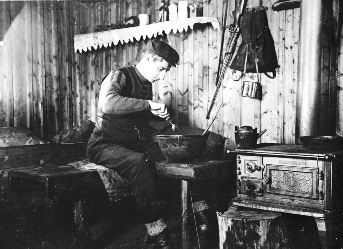 Anno Domkirkeodden, Simen Baardseth, spiser av jerngryte, interiør, hytte, ovn fra Aadals Brug, rifle på veggen, kaptein Skaugs hytte, Gammelskolla seter, Ringsakerfjellet.