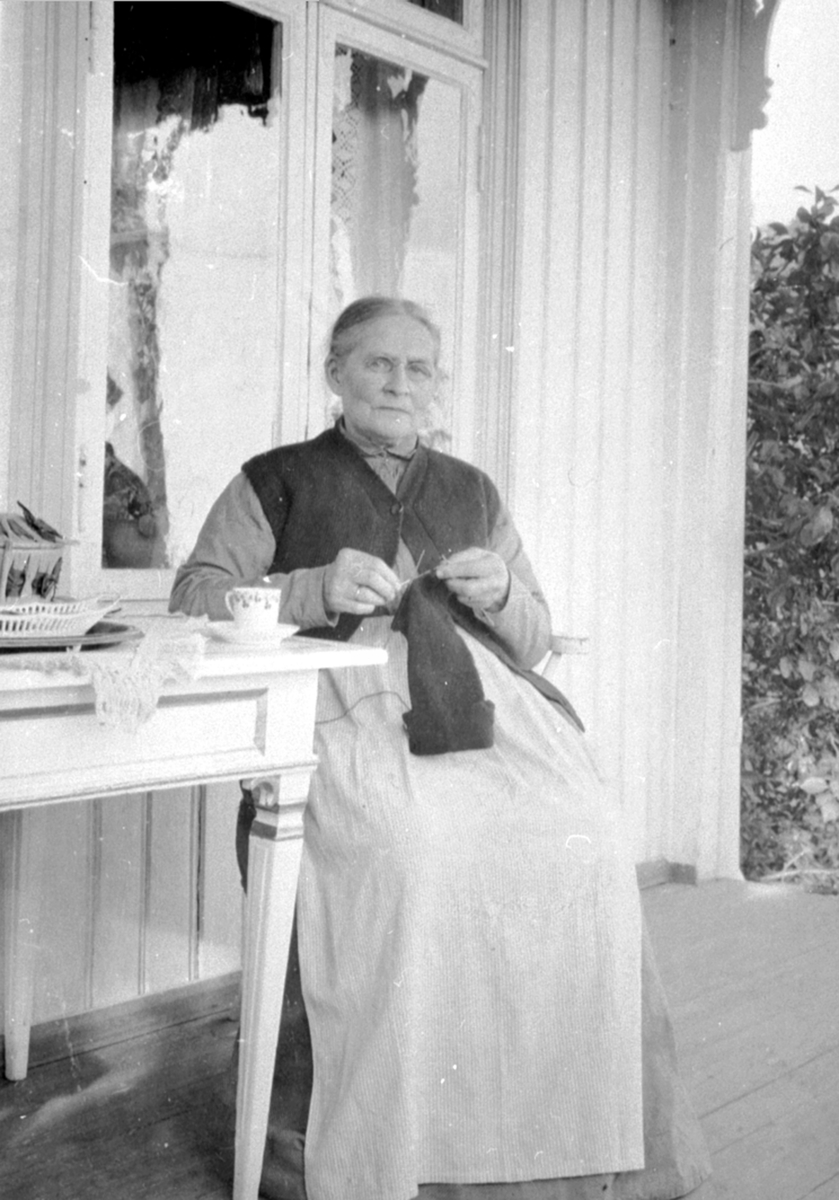 Anno Domkirkeodden, Agnethe Heramb født Rindal, sitter på veranda og strikker. Heramb, Gaupen, Ringsaker.