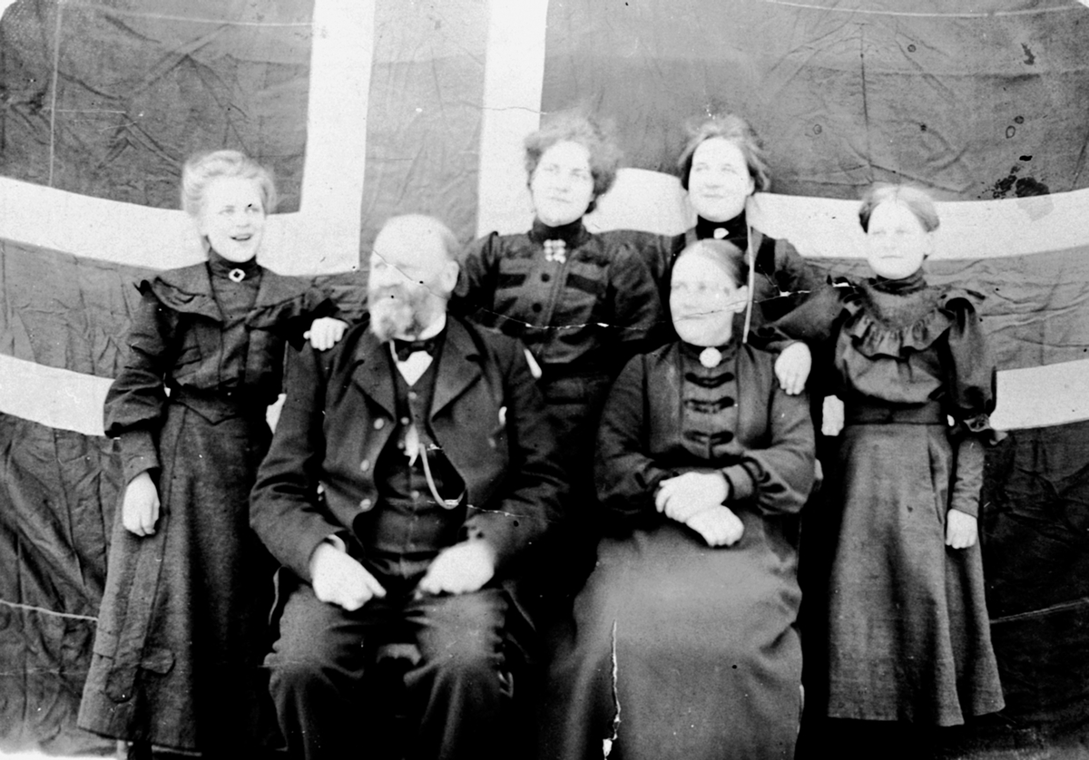 Anno Domkirkeodden, Familien Simenstad foran det norske flagget. Foran Ansten f.1852, Dina Ingeborg f.1861. Bak fra venstre er Kristine f.1891, Grethe f.1888, Dorthea f.1890, Julie f.1894. Simenstad, Veldre, Ringsaker.