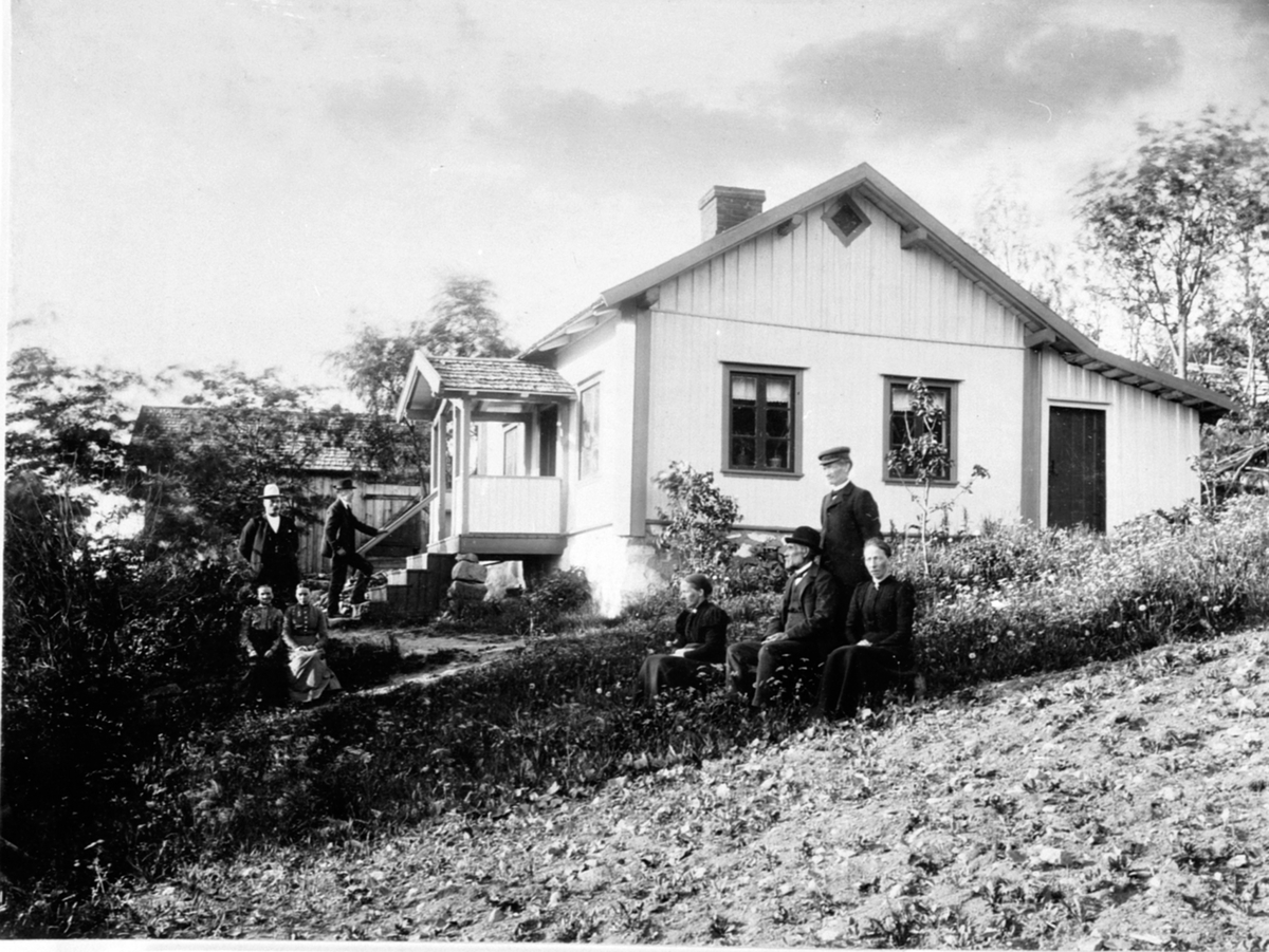 Anno Domkirkeodden, Gruppe personer foran hus. Fra venstre er Mathea Bekkevold, husholder hos lære Skaug Marie Lerbakken, Syljuåsen. Bak er lærer Nikolai Skaug med hatt, i trappa er Andreas Bekkevold, sittende er Eline Vestli, Ole Olestad, Eline Hagen, bestefar Even Bye, Olstad ved Nordheim, Ring, Ringsaker.