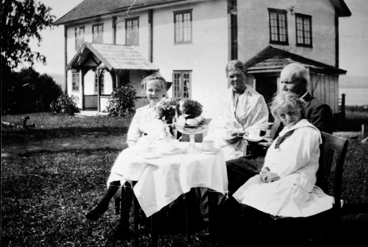 Anno Domkirkeodden, Otilie Torsdatter Fjell (1855-1927) og Kristian Andersen Bratberg (1860-1932) sammen med 2 tyske jenter. Dekket kaffebord foran hovedbygningen på Fjell, Helgøya. Rappet hovedbygning.