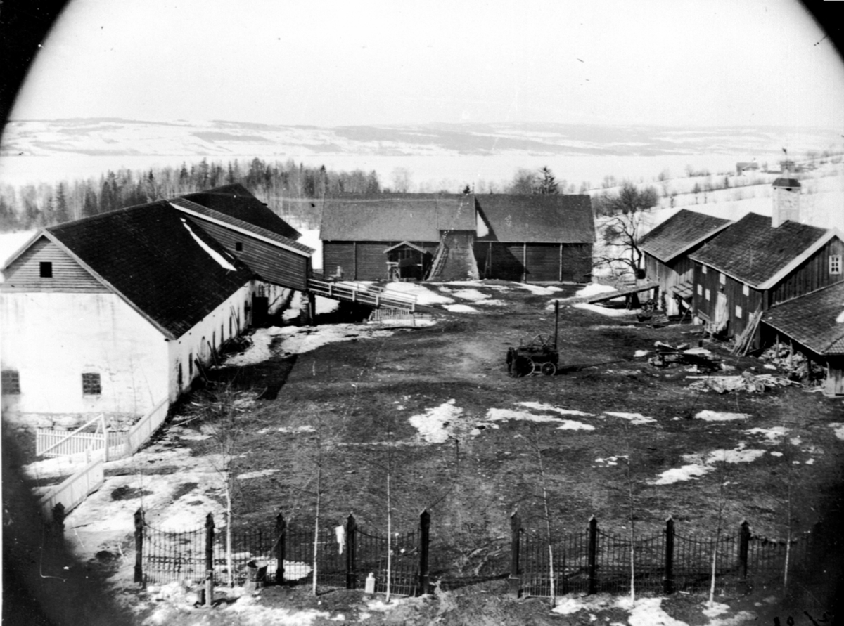 Anno Domkirkeodden, Utsikt mot gårdsplassen på Hovinsholm, Helgøya. Stall og fjøslåve til venstre, låve rett frem, stabbur og uthus til høyre. Lokomobil på plassen. Kan skimte husa på nedlagte gården Kval i bakgrunnen.