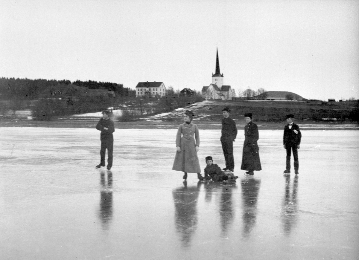 Anno Domkirkeodden, Skøyteløpere på Mjøsisen. Ringsaker kirke og prestegarden i bakgrunnen. Damene kan være døtre av sogneprest Brockmann.