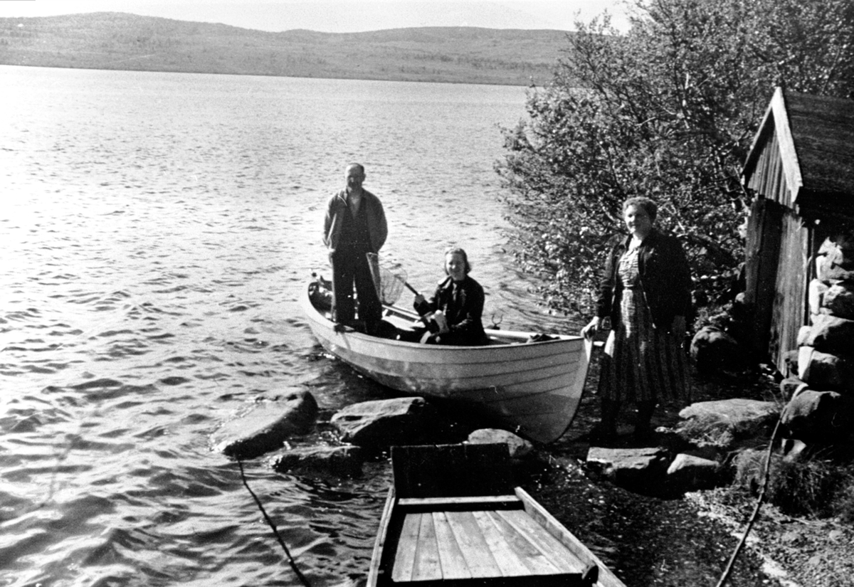 Anno Domkirkeodden, Fisketur i robåt på Grunna, Ringsaker Almenning. Ombord i båten er Even Mengshoel og Helene Hauger. Ved båthuset er Agnes Mengshoel.