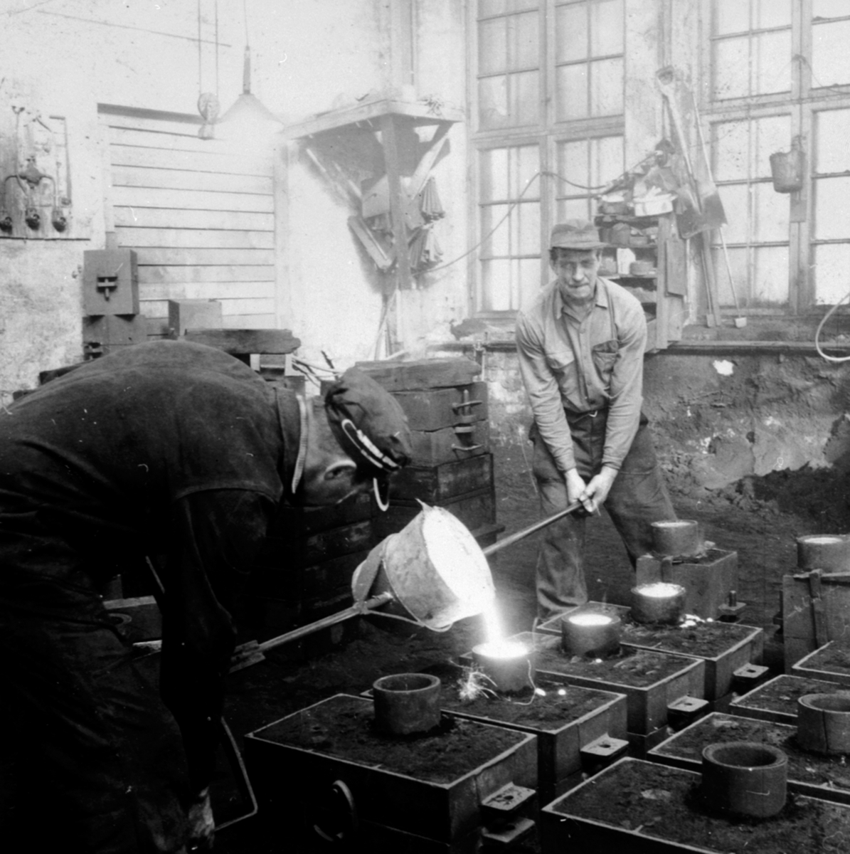 Anno Domkirkeodden, 2 arbeidere heller flytende smeltemasse i former ved A/S Moelven Jernstøperi.