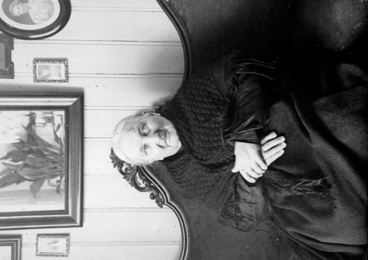 Anno Domkirkeodden, Portrett, ukjent gammel dame som sitter på sofa, fotografier på veggen, Ringsaker (Hjelt?).