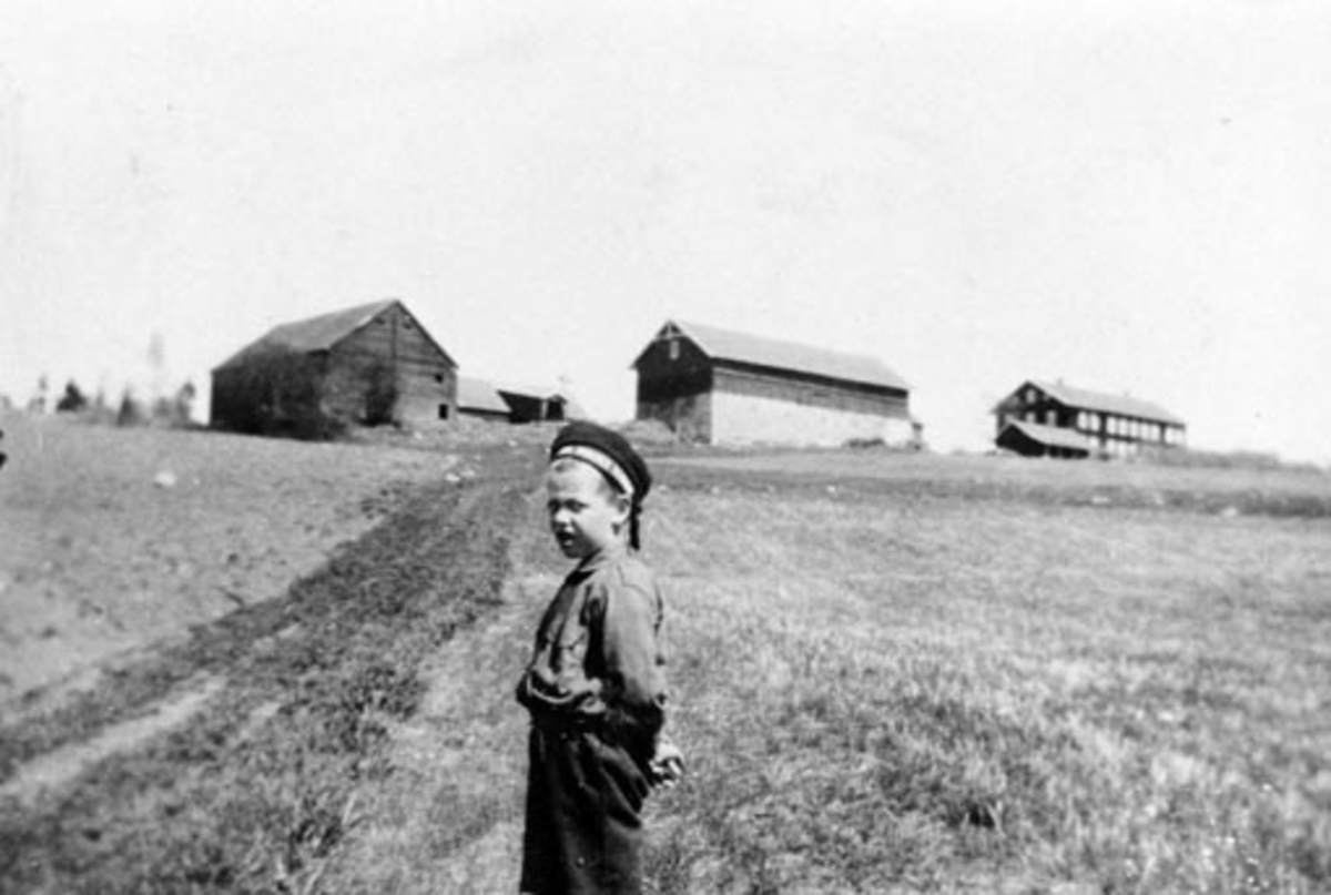Anno Domkirkeodden, Garden Fossum, Nes, Hedmark med gamle uthus. Hovedbygningen ble bygd ny etter brann i 1871, men stod ikke ferdig før 1880. Det er Erling Feiring f.1915 som står i forgrunnen.