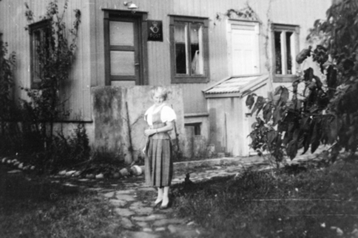 Anno Domkirkeodden, Boligen Libo, Smedstuen nedre, Nes, Hedmark. Smedstua poståpneri fra 1914 til det ble flyttet ned til Smedstuen Brygge. På bildet er poståpner og landpostbud Mary Lie (1898-1981) i bunad. Posthusmerke på døra.