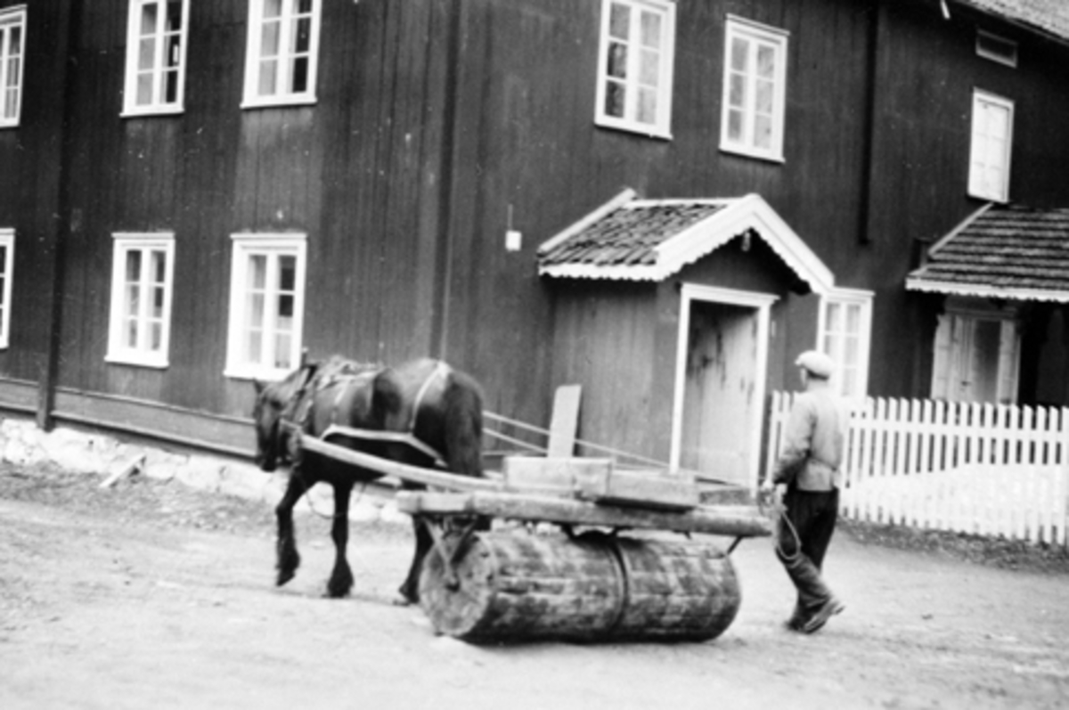 Anno Domkirkeodden, Eksteriør. Hovedbygningen på Dæli, Brøttum, Ringsaker. Mann med hest og åkerrulle på tunet.