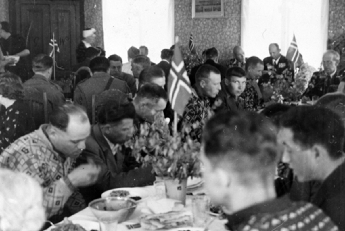 Anno Domkirkeodden, Interiør, stue, Vetten gård, Jessnes, Ringsaker. Mange menn spiser lapskaus, russiske krigsfanger, bord pyntet med lauv og norske flagg.