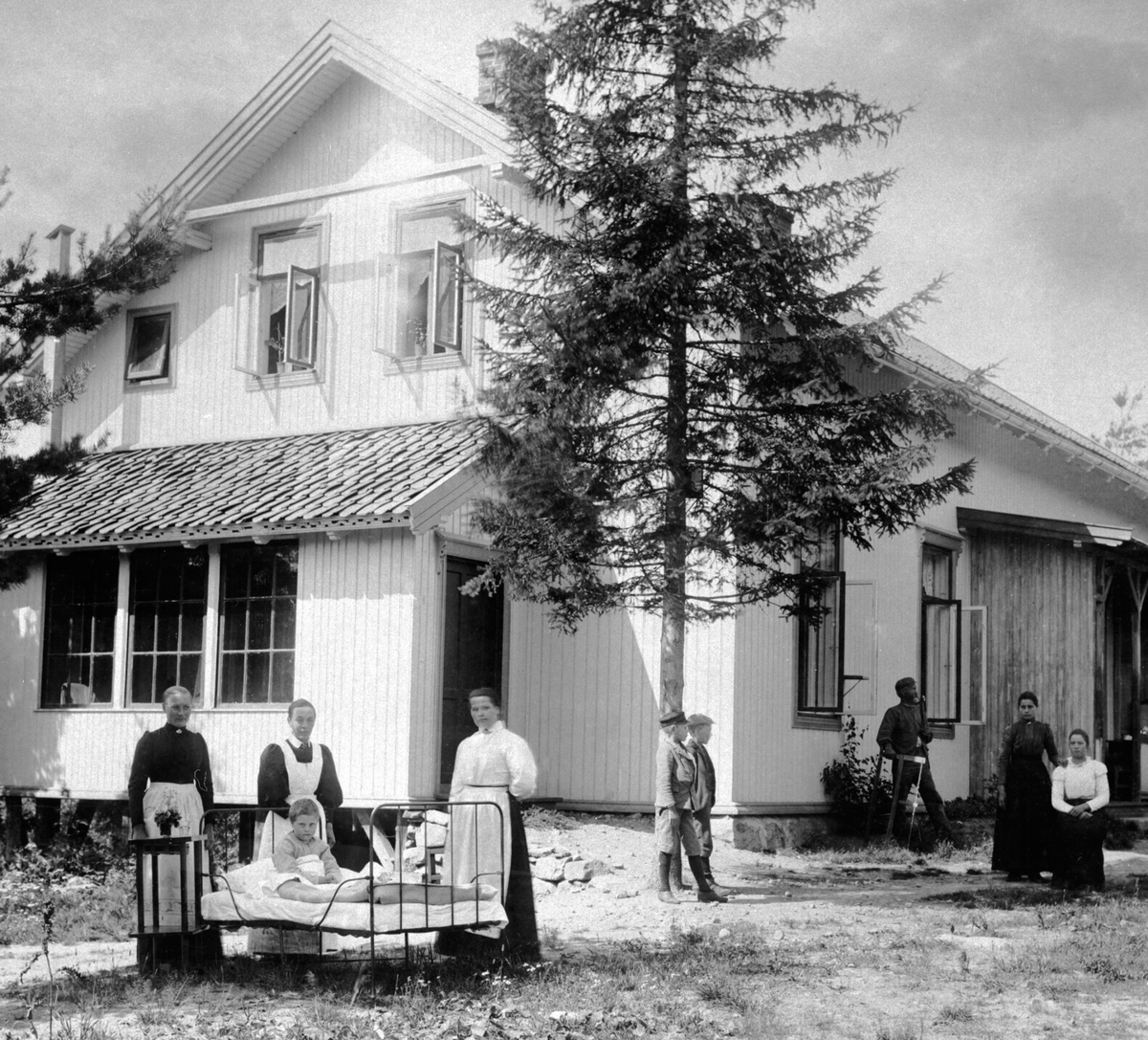 Anno Domkirkeodden, Ringsaker Sykehus, bygget 1895, men kom ikke i drift før 2 år senere. Her med pasienter og pleier utenfor. I midten bak senga er bestyrerinne Syverine Harby. Huset ble revet i 1951 for å gi plass til herredshuset.