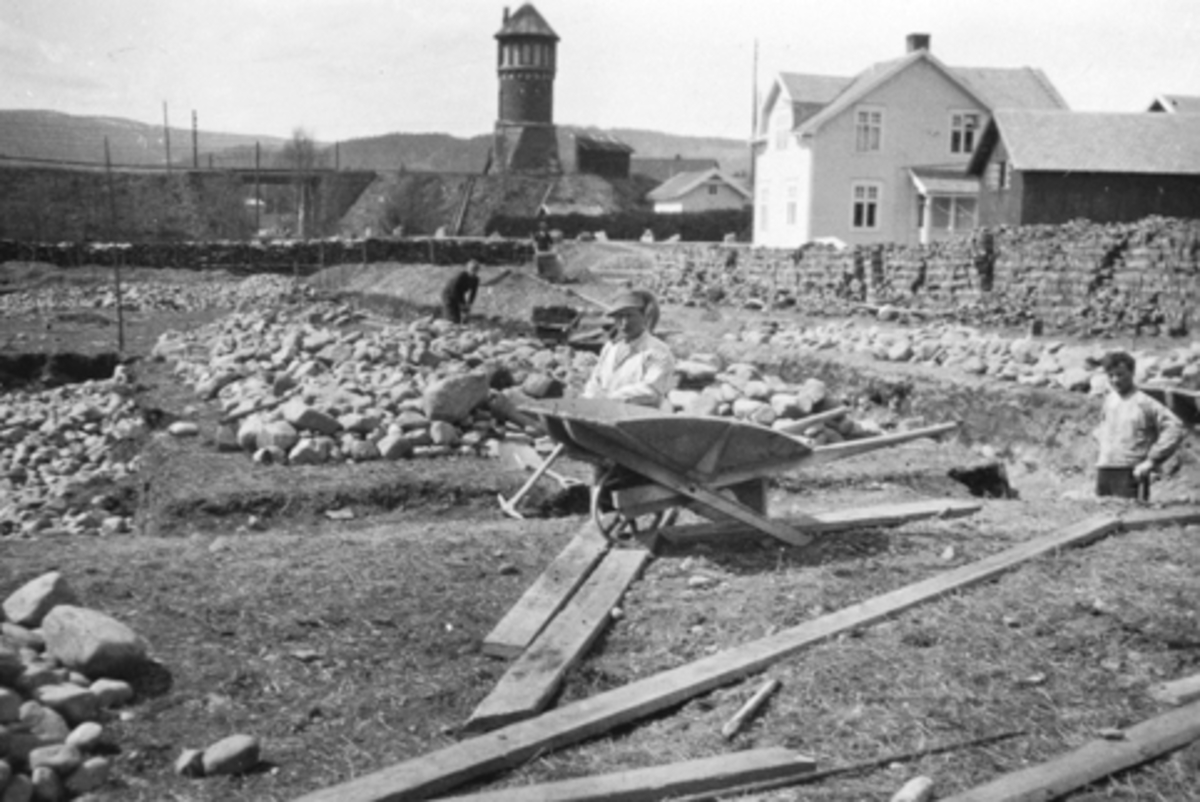 Anno Domkirkeodden, Bruvold mølle, Moelv, Ringsaker. Hans Sundgaards lærfabrikk. Bygging av fabrikken, arbeidere på tomta, trillebår. I bakgrunn er vanntårnet på Moelv stasjon.