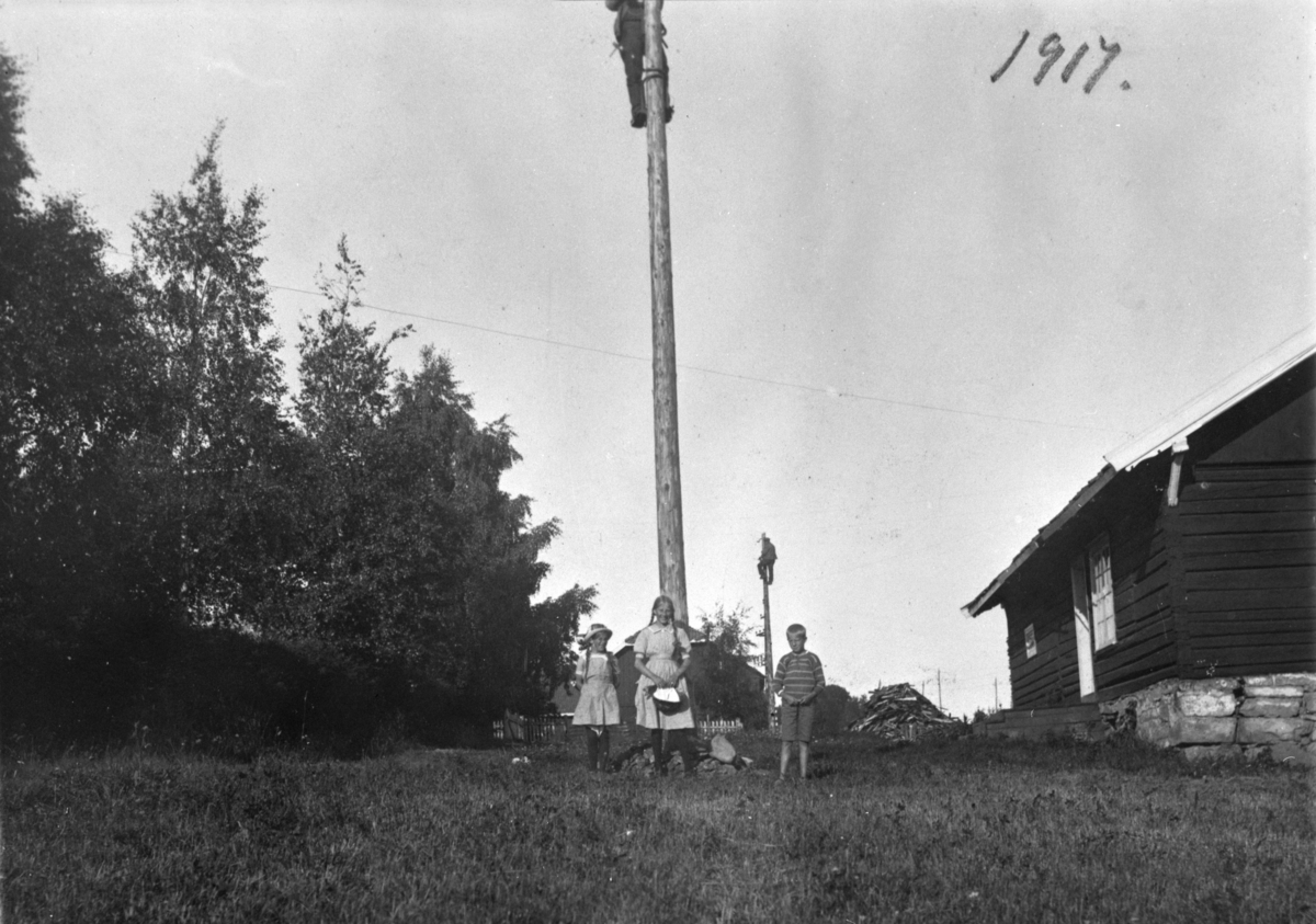 Ukjent, Kraftlinjer i Ringsaker 1917. Menn fra kraftselskapet i klatresko i strømstolper. Ukjente barn i forgrunnen.