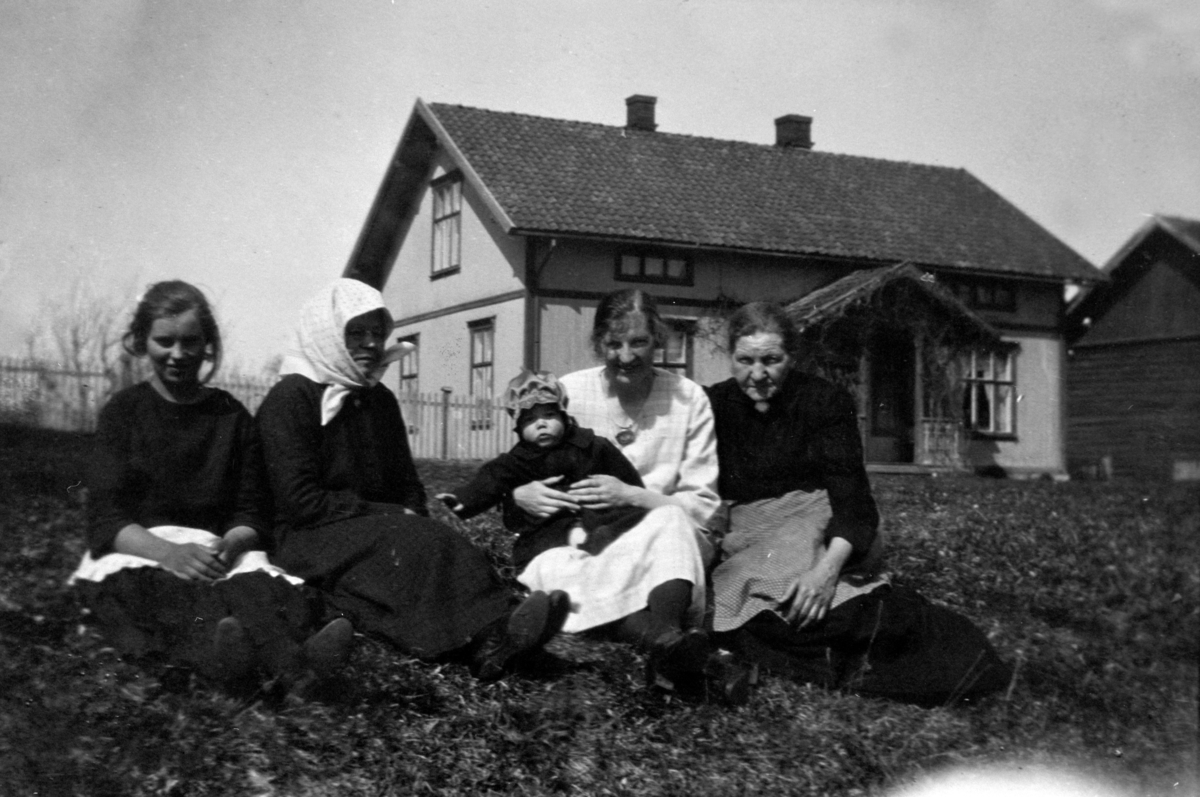 Anno Domkirkeodden, Oppgitt av giver, 1982, som bilde fra Farmen skole ca 1915, antatt lærerboligen. Samme motiv 0414-06963 er oppgitt som bilde fra Vang klokkergård, 1920-tallet. Fire kvinner og et lite barn sittende i gresset foran en bygning.