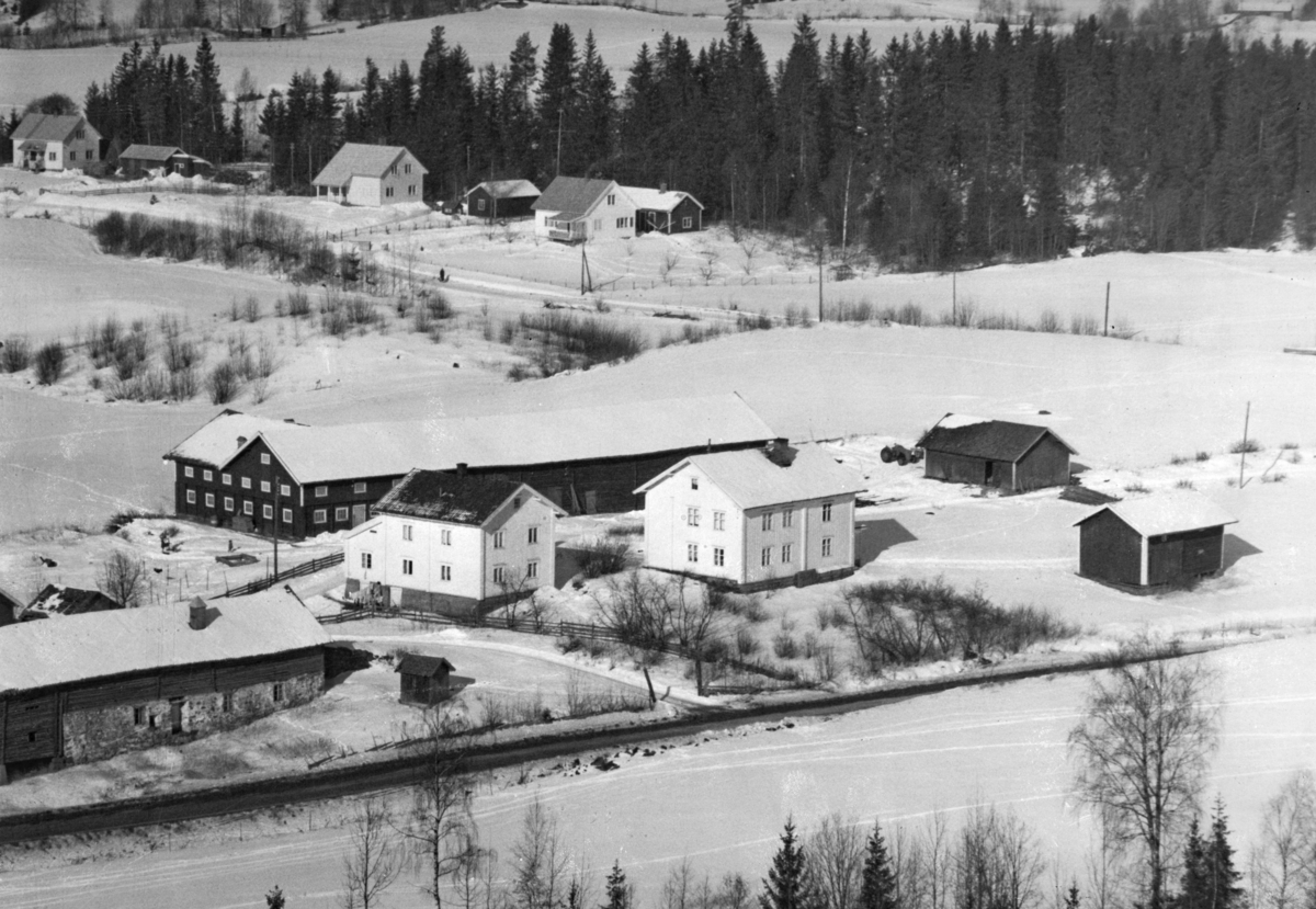 Ukjent, Flyfoto Øvre Slemsrud i 1950-årene. Nederst ser vi deler av fjøset og låven på Nedre Slemsrud. Gardsvegen til Nedre Slemsrud går mellom låven på Nerigarden og bygningene i oppigarden. Bildet viser elllers tunet på Øvre Slemsrud med den gamle tømrede låven med det nye fjøset, den vesle bygningen, ho…