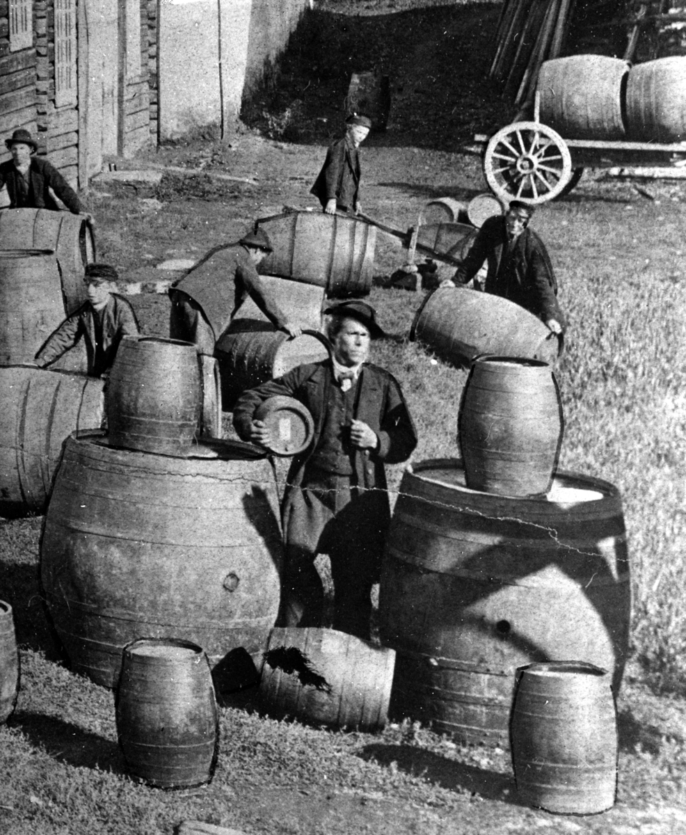 Normann Fotoatelier, Løiten Brenneri, Løten. Brenneriarbeidere, eiketønner, fat, ukjent mann med 40 potters anker under armen. Normann repro NR-6335.
