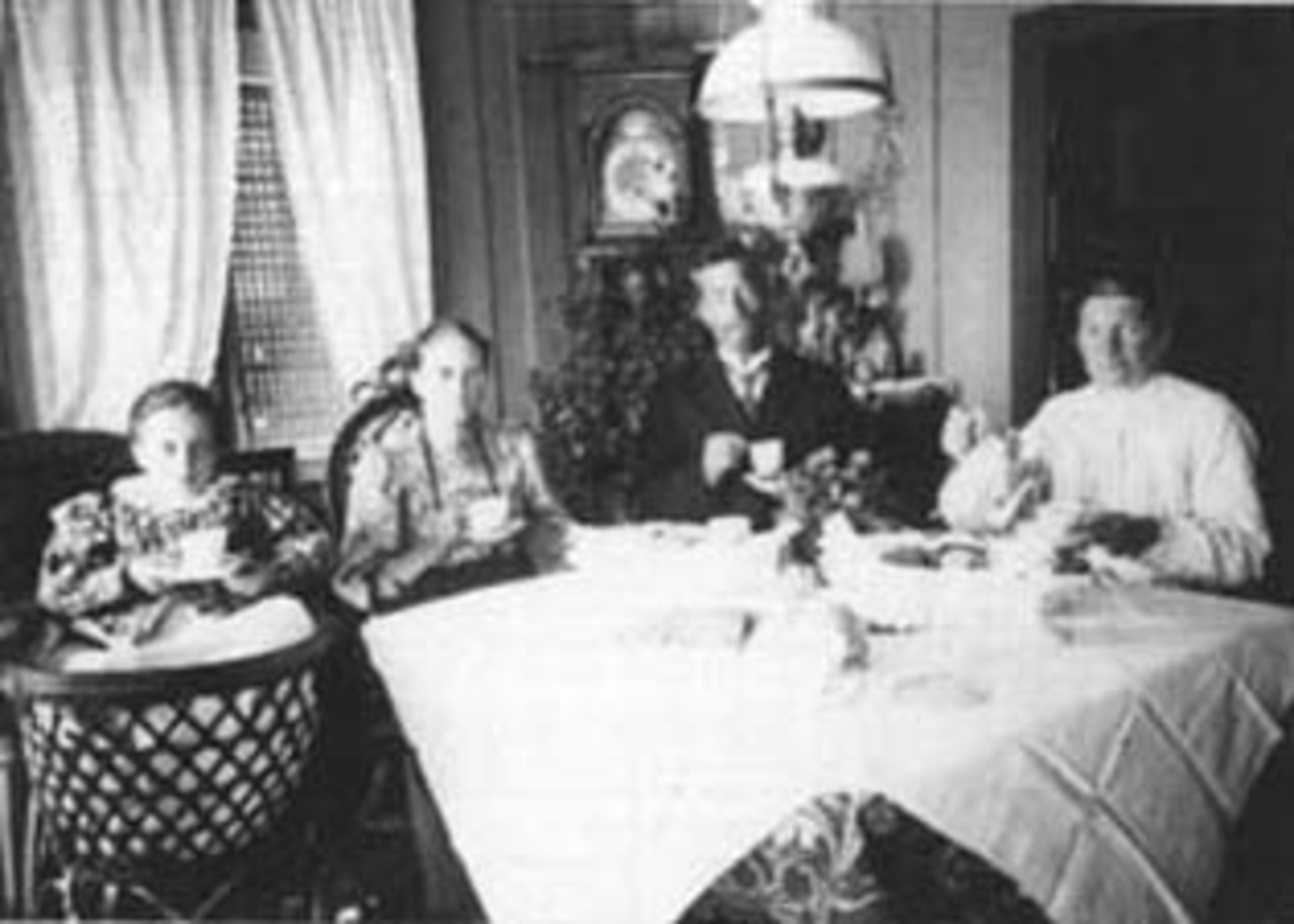 Normann Helger, INTERIØR: STUE, GRUPPE: 4 RUDT KAFFEBORD, 3 VOKSNE, 1 SYK PIKE I "BARNE-VOGN", KURVVOGN MED STOLRYGG, PARAFINLAMPE, HAUKAASEN NORDRE. Haukaasen Nordre, før 1911. Fra venstre: Marte Petersdatter Haukåsen (1897-1911), Lisa Halvorsdatter Haraset (1871-1952), Peter/Per Olsen Haukåsen (1869-1923), Margr…