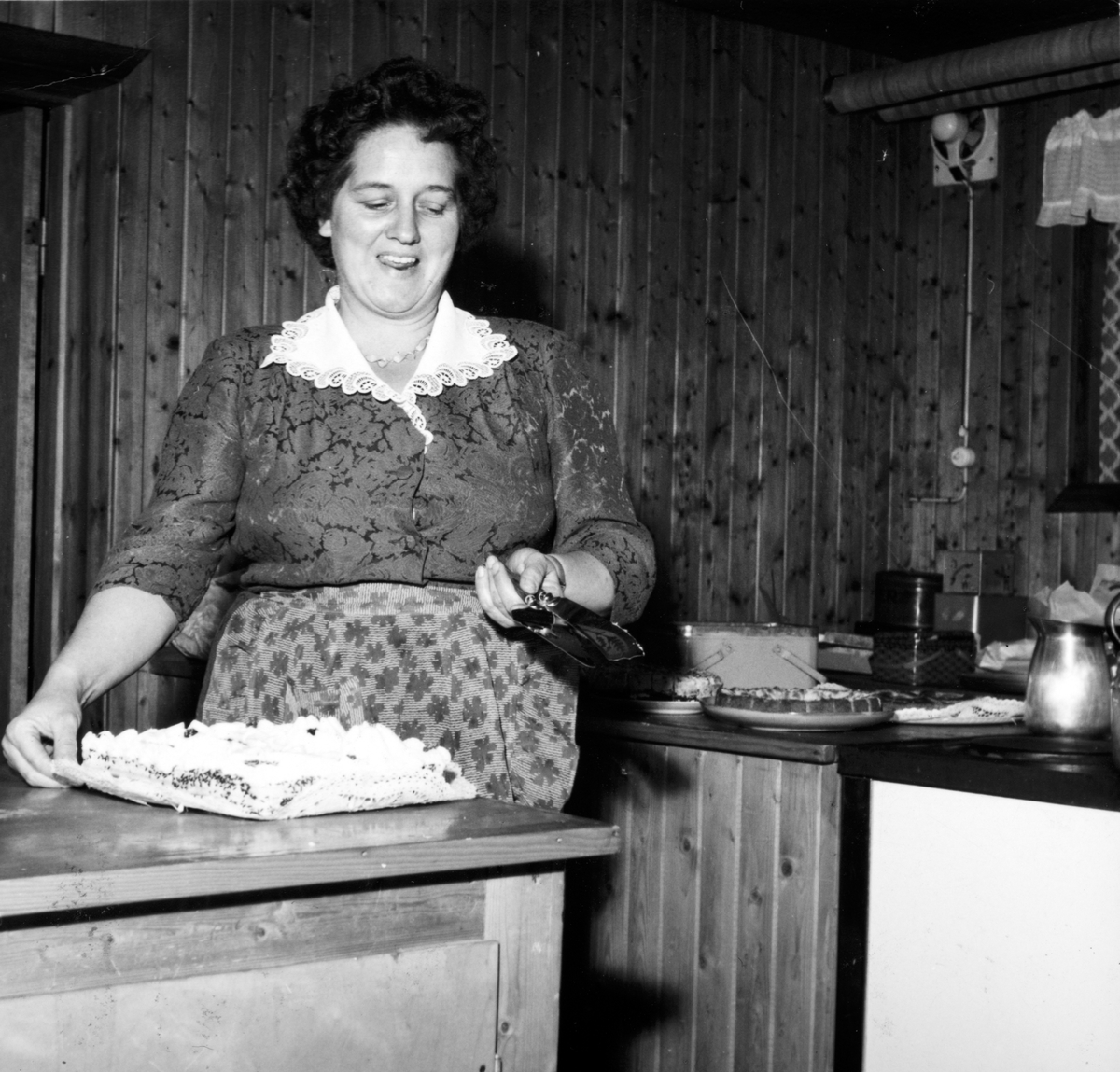 Ukjent, Nordvang forsamlingslokale på Espa i Stange. Danseskole. Paula Johnsen skjærer opp kake på kjøkkenet på Nordvang på danseskoleavslutning i 1955.