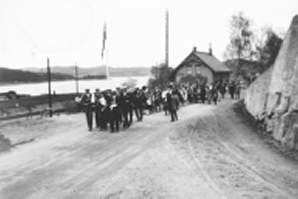 Ukjent, Espa, Stange. 17. mai-toget med Espa Musikkorps i spissen marsjerer forbi Espa Jernbanestasjon i 1932