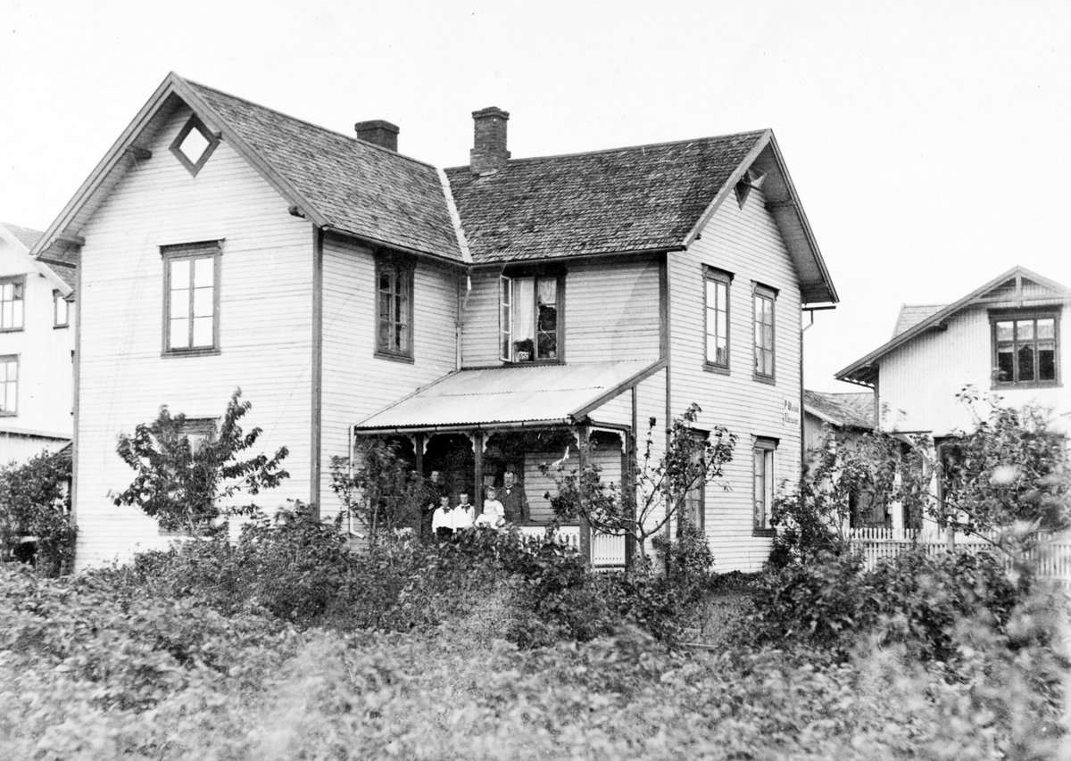 Ukjent, Gaarder, østre, Storgata i Stange. Huset til urmaker Peter Ottestad ca. 1903. Huset brant i 1911. På verandaen ekteparet Julie og Peter Ottestad og barna Erling, Marcus og Aagot. Gr. nr. 96-22. Flere opplysninger se boka "Handelsforretninger i Stangeby`n med omegn" skrevet av Jan Arne Berg, utgitt …