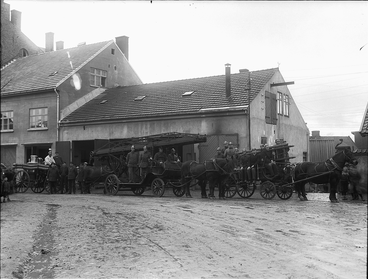 Christian Grundseth, Hamar brannstasjon i Grønnegata 70 sto ferdig i 1897 og ble utvidet i 1920-åra. Fv: Ei vogn med dampdrevet sprøyte, i midten en stigevogn med gassdrevet reising av stigen. Hestevogner, brannmenn. Dette bildet ble tatt i forbindelse med utskifting fra hestetrukne vogner til biler. Se 0401-02407.