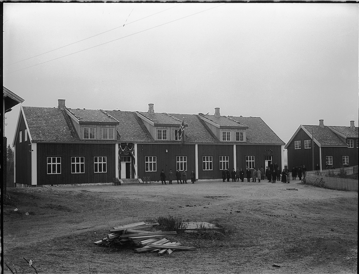 Christian Grundseth, HAMAR JERNBANESKOLE. DISEN. EKSTERIØR. FOLK PÅ TUNET. JUST BROCHSGATE 13. Skolebygningen ses til venstre, lærerboligen til høyre. Bildet er antagelig tatt på åpningsdagen 1. november, 1920. Pyntet med norske flagg.