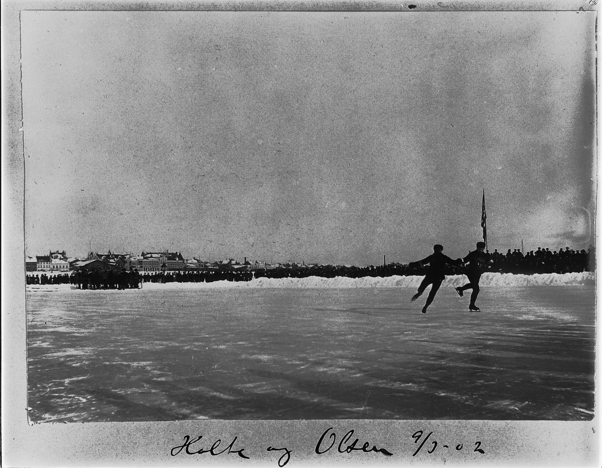 Johan Albert Steen, SKØYTELØP PÅ MJØSISEN, KUNSTLØP, HOLTE OG OLSEN, TRIBUNE, PUBLIKUM, FLAGG, 9-3-1902, BEBYGGELSEN I STRANDGATA, HAMAR I BAKGRUNNEN.