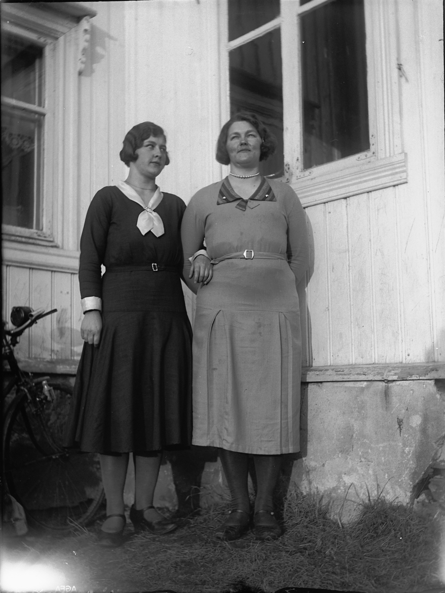 Ole M Martinsen, To ukjente kvinner foran et hus. Sykkel lent inntil en vegg.