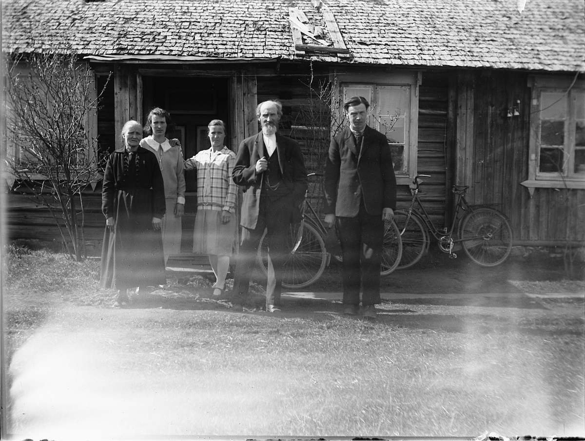 Ole M Martinsen, Ukjent gruppe, familie foran inngangen til et ukjent hus. To sykler ved husveggen. Spånestad midtre, Løten, fotografens barndomshjem.
