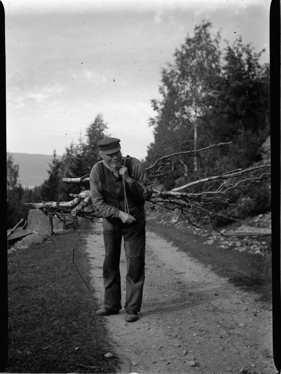 Mikkel Sveinhaug, FØDERÅDSMANNEN PÅ KLØVSTAD, BRØTTUM i Ringsaker HENTER BRENSEL, VED, BÆRER KVIST PÅ RYGGEN MED TAU OVER SKULDRA.
