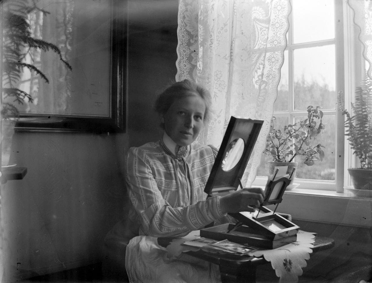 Ole Hansen Løken, ANTONETTE HERSOUG SER PÅ FOTOGRAFIER GJENNOM ET BETRAKNINGSAPPARAT, MED LUPE.