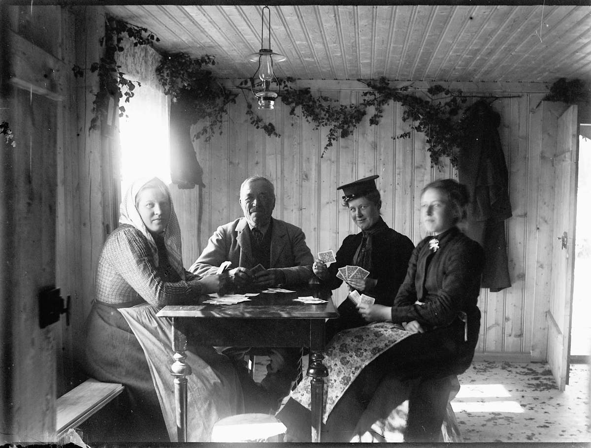 Ole Hansen Løken, GAMMELSKOLLA, INTERIØR 4 PERSONER RUNDT BORD SPILLER KORT. KORTSPILL. F. V. MIMMI LØKEN, UKJENT, FRU KUNSTMALER SUSI PETERS, ANTONETTE HERSOUG, FØDT RING.