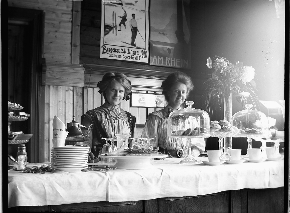 Ole Hansen Løken, TO UKJENTE KVINNER, KAFFE OG KAKER. KAKEFAT, KOPPER. JERNBANEKAFEEN PÅ RINGEBU JERNBANESTASJON. 1910-15.