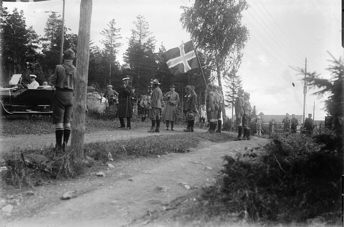 Oscar Løberg, SPEIDERE PÅ LANDSLEIR PÅ STORHAMAR 1924, KONG HAAKON SVARTKLEDD MED HVIT LUE, NÆRMEST HAM SPEIDERSJEF H. MØLLER GASMANN OG FYLKESMANN ØYEN. NORSK FLAGG.