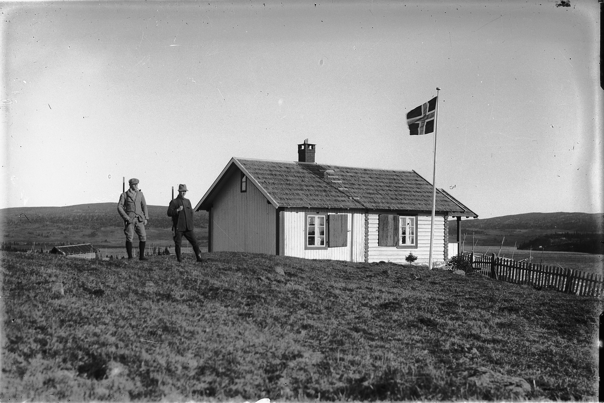Oscar Løberg, TO JEGERE VED HYTTE, UKJENT STED, NORSK FLAGG.