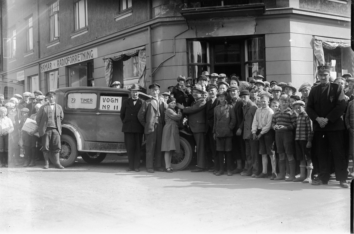Oscar Løberg, "Pålitelighetsløp" til Ford-forhandlere i 1931, billøp i Hamar som en del av markedsføring av produktene sine, folkemengde og bil utenfor Oplandske Auto i Torggata 13, Hamar. Folk kunne tippe hvor mange kilometer bilen ville tilbakelegge i løpet av tre døgn, vinnerne ble premiert i form av bilturer.
