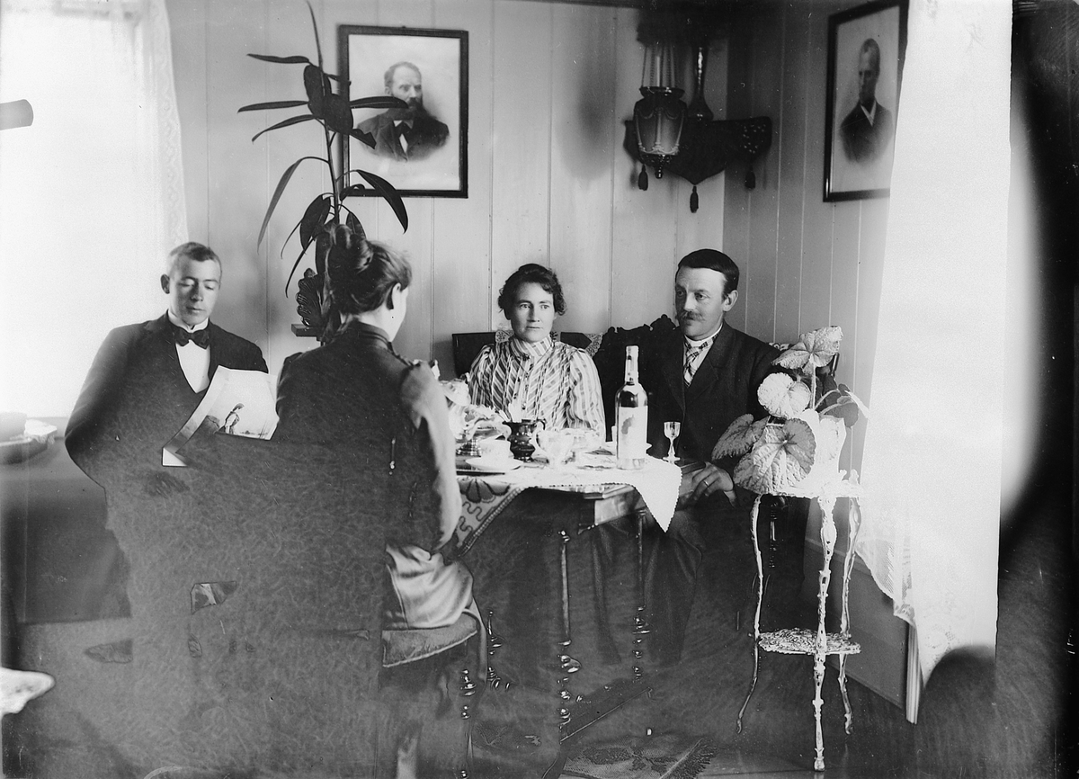 Mina Skraastad, To menn og to kvinner drikker kaffe, dram, ved et stuebord. Interiør, stue.
