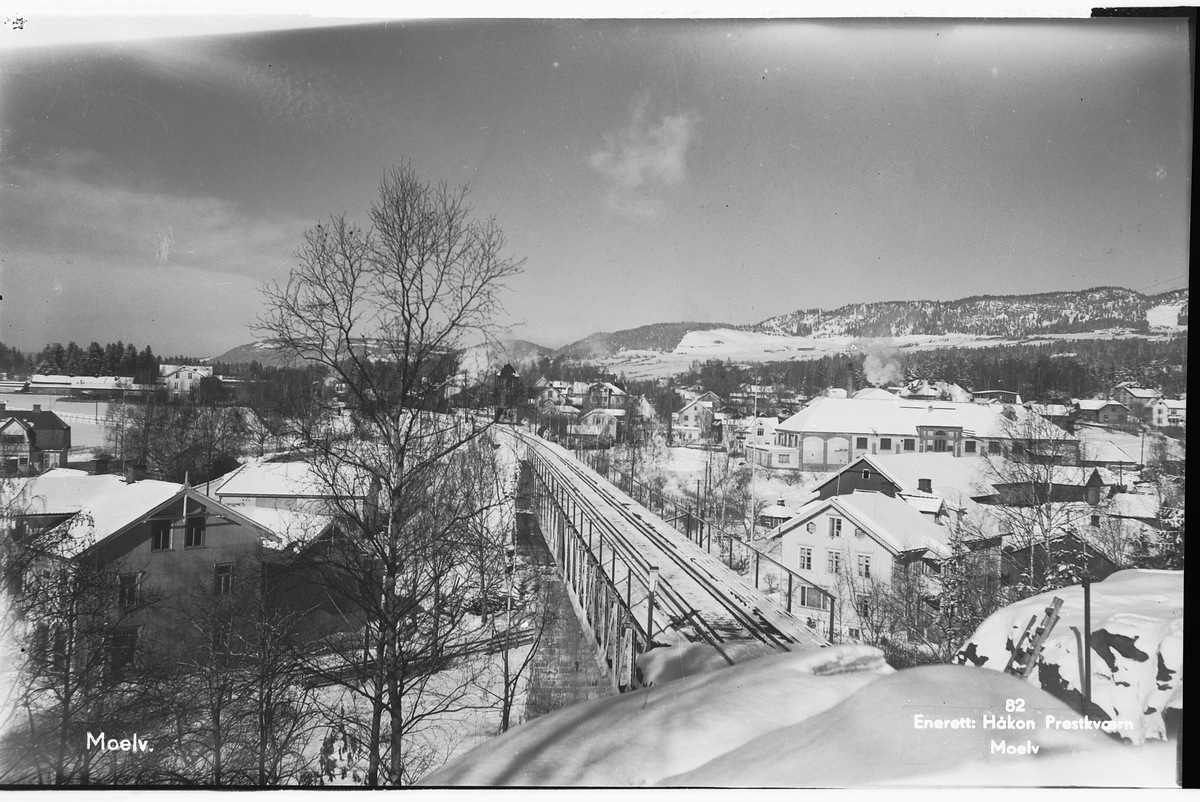 Håkon Prestkværn, Postkort Moelv. Foto Håkon Prestkværn, Moelv. No. 82. Sett fra Dehliberget. Jernbanebrua over Moelva. T. v. Linnerud og t. h. Brovold. Moelv sentrum i bakgrunnen. Vinter. 1962.