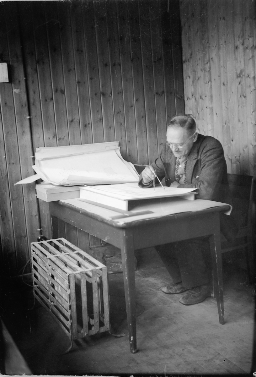 Håkon Prestkværn, STRAND BRÆNDERI i Ringsaker, BRENNERI, VÅREN 1947. INGENIØR BIRGER LARSEN VED TEGNEBRETT. ELEKTRISK VARMEOVN? PÅ GULVET.