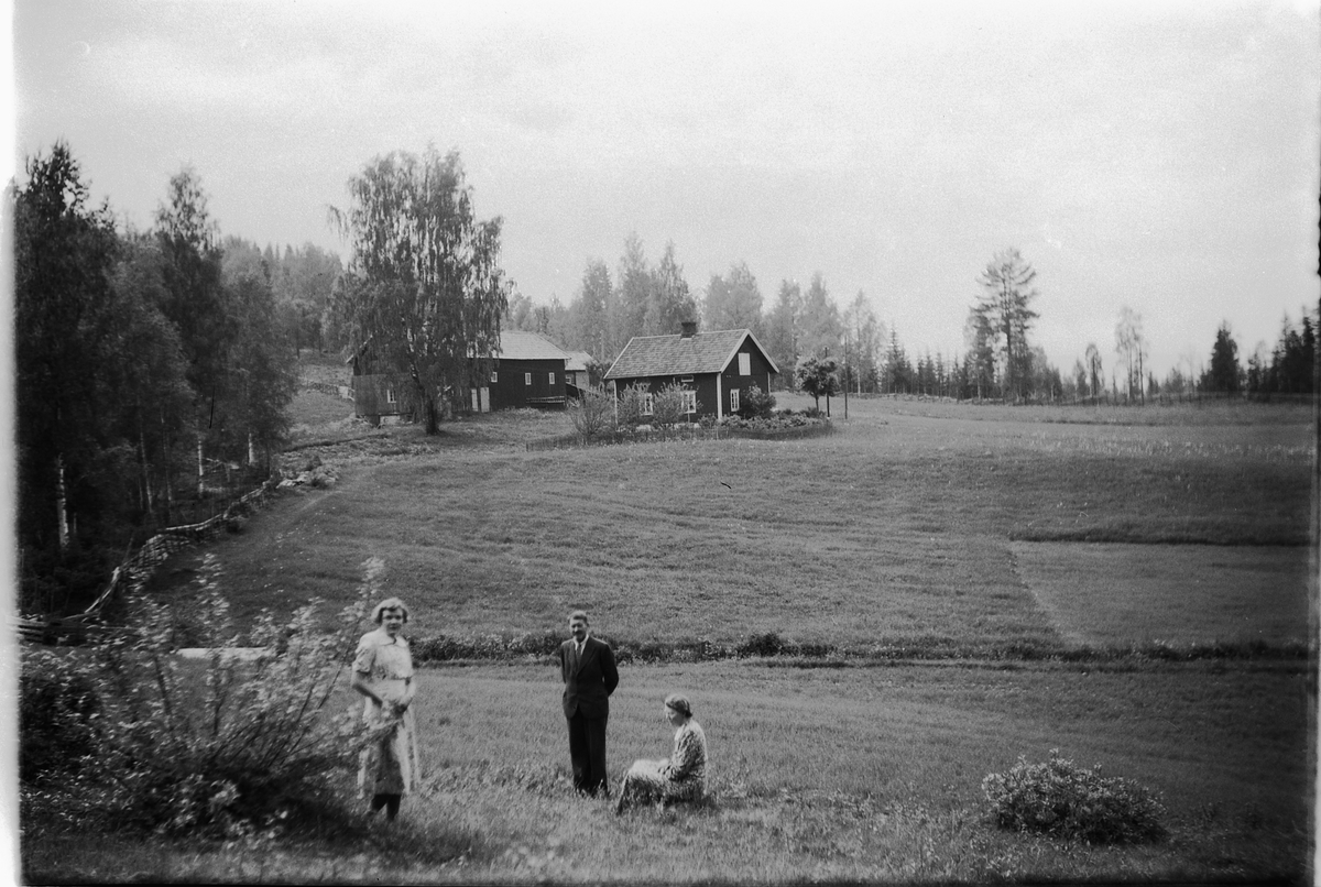 Håkon Prestkværn, To ukjente kvinner og en mann foran et jorde og gard. Mannen er byggmester Nils Haug og garden er Bækkelund i Næroset