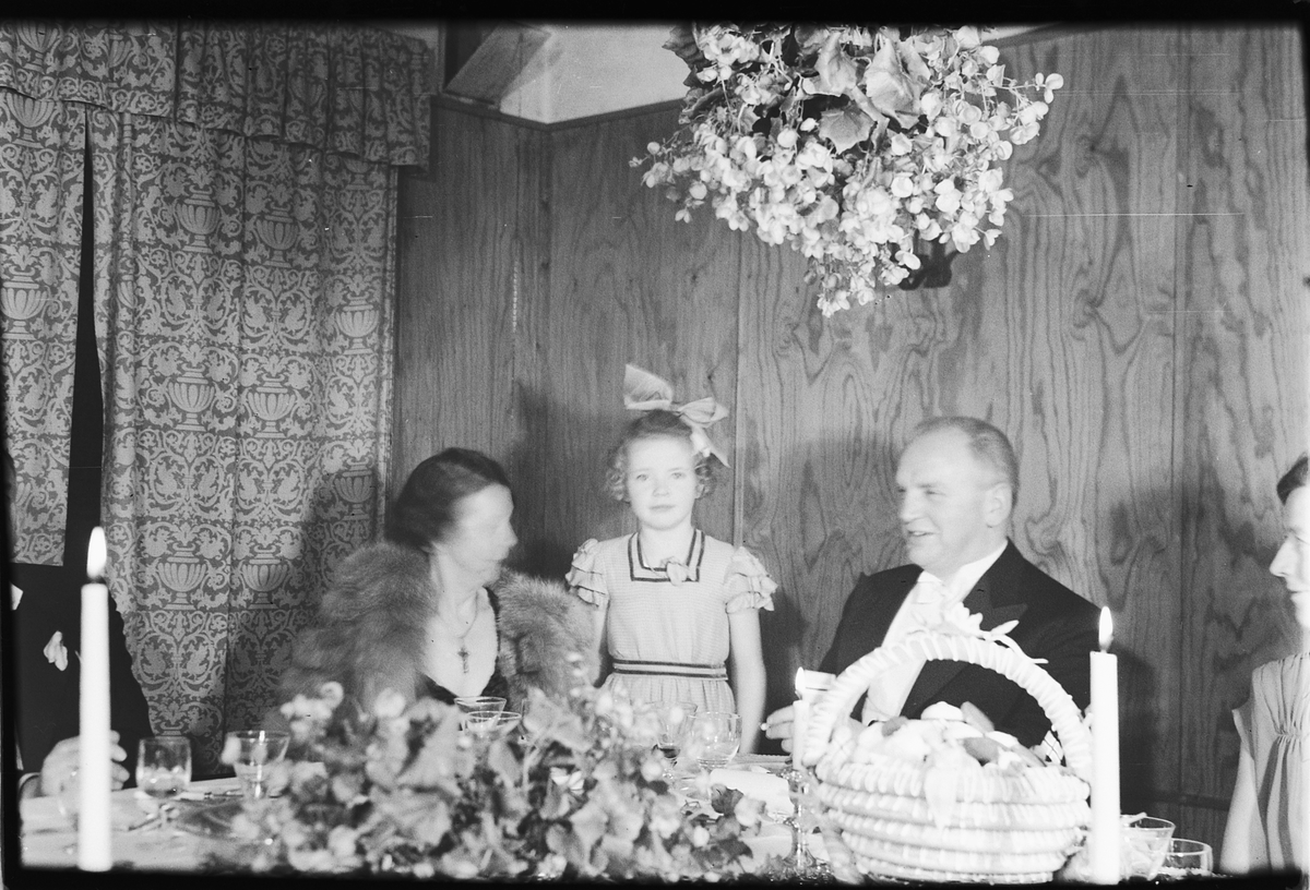 Håkon Prestkværn, Arendal, sølvbryllup. Ukjente personer ved pyntet bord, pike med sløyfe står bakerst.