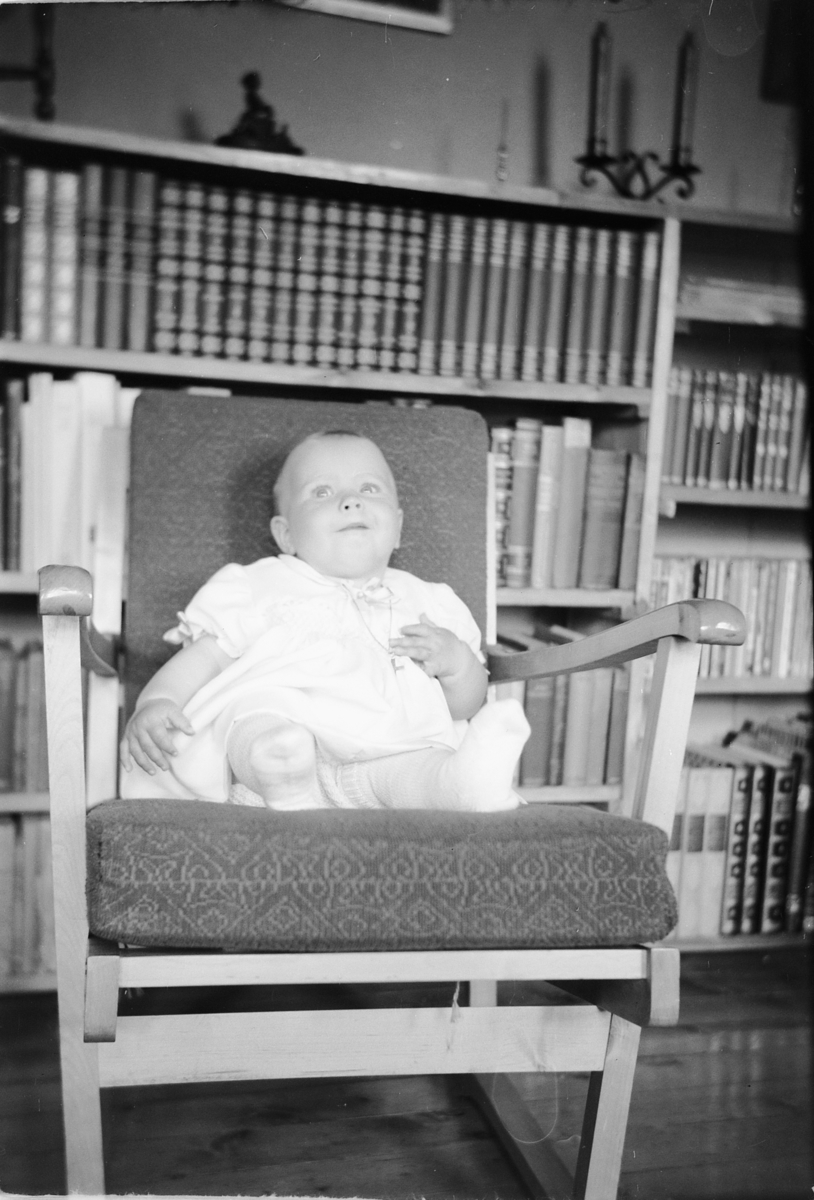 Håkon Prestkværn, En baby sitter i en stol foran en bokhylle.
