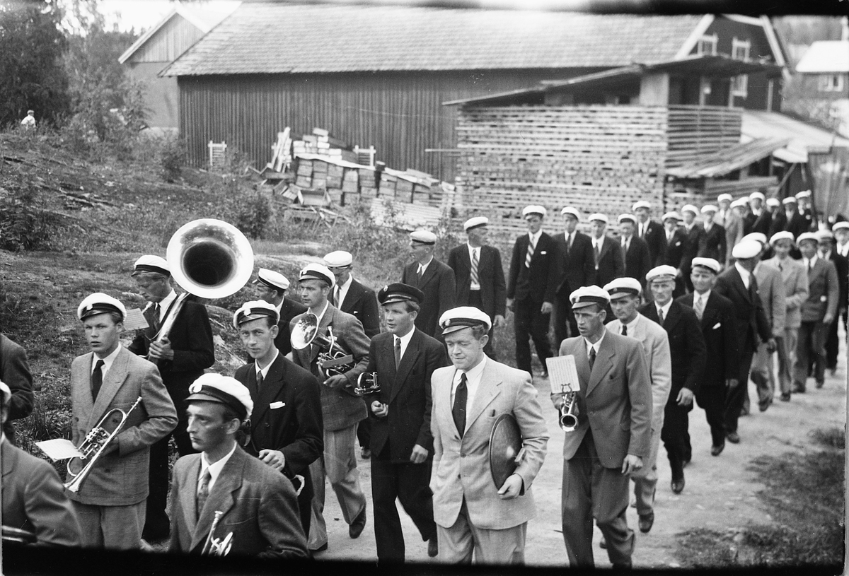 Håkon Prestkværn, Musikkorps går i tog. Dette er Næren Musikkforening fulgt av Næren Mannskor. Oppmarsj i Parkvegen forbi Johansens snekkerfabrikk. Ringsaker sang- og musikklagsstevne, Moelv 1948 (eller 1952). Friluftskonserten i Folkets Hus park.