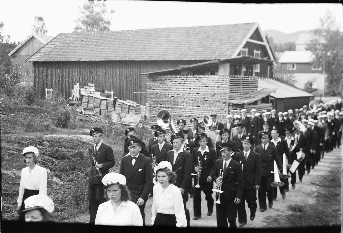 Håkon Prestkværn, Musikkorps går i tog. Ringsaker sang- og musikklagsstevne, Moelv 1948. Oppmarsj forbi Johansens trevarefabrikk.