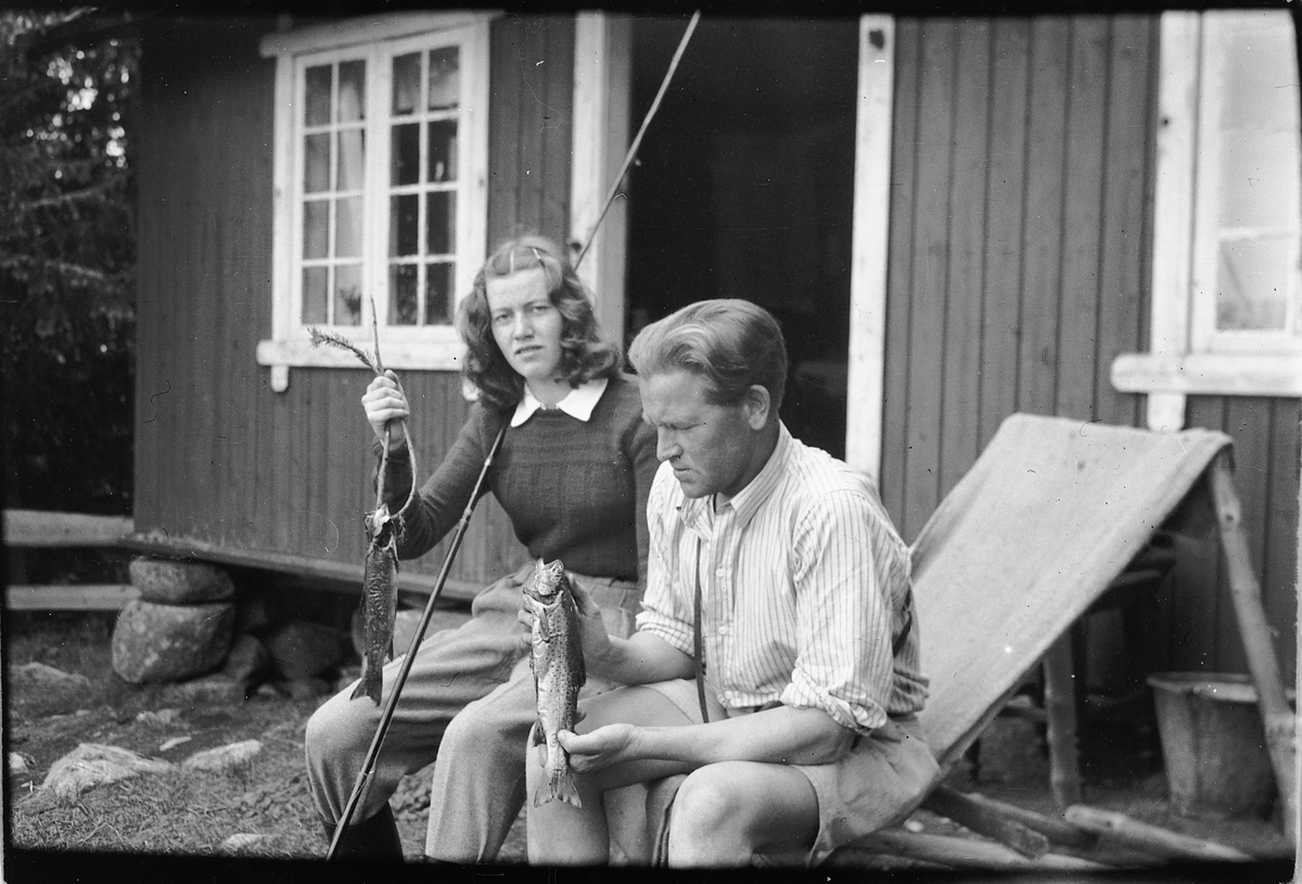 Håkon Prestkværn, Ei kvinne og mann ved ei hytte viser frem to ørret etter en fisketur.