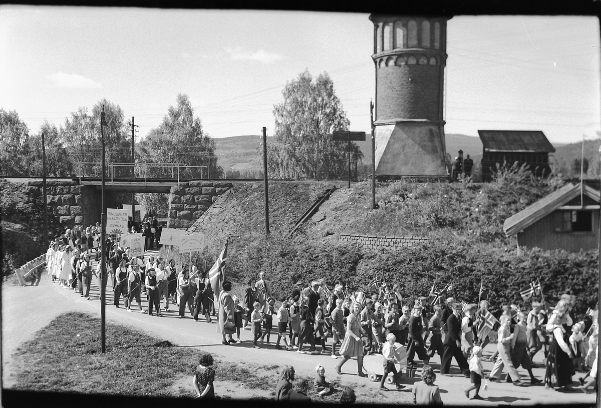 Håkon Prestkværn, 17. mai-tog i Storgata, Moelv. Vanntårnet ved Moelv jernbanestasjon i bakgrunnen.