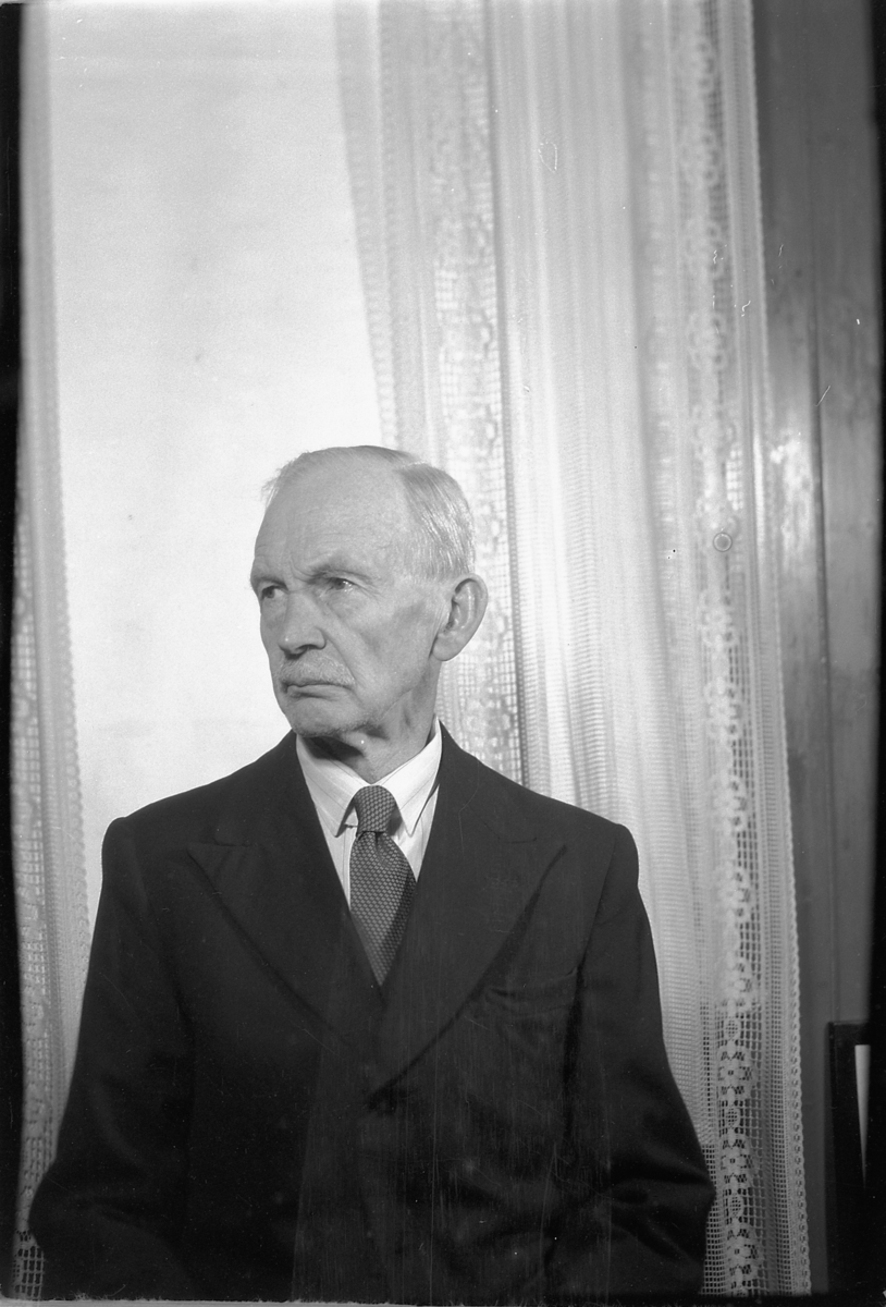 Håkon Prestkværn, Eldre mann foran vindu med gardiner.