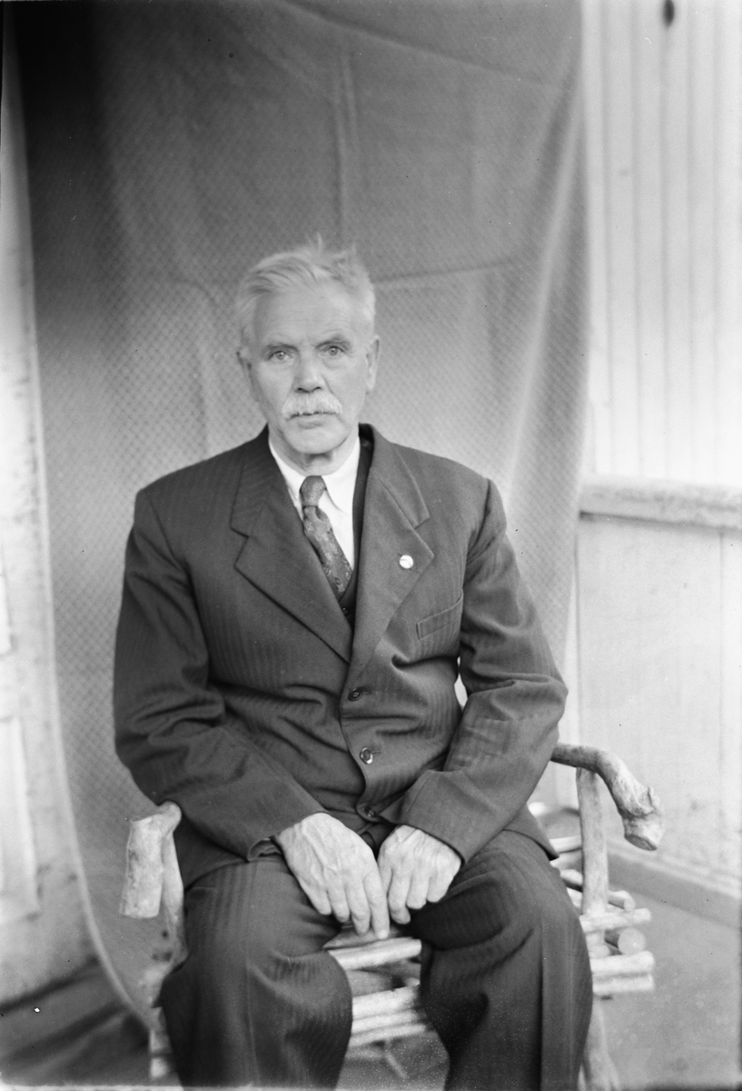 Håkon Prestkværn, Eldre mann i dress sitter på en stol.