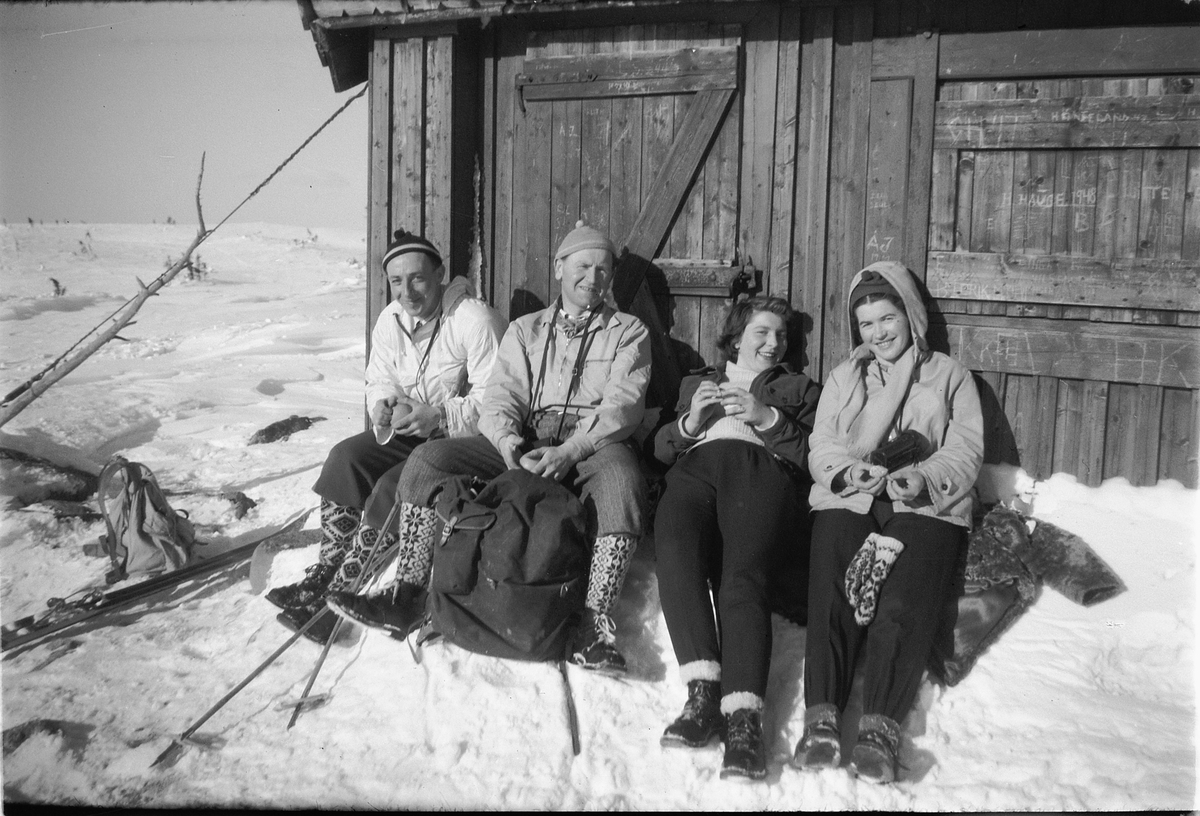 Håkon Prestkværn, Vinter. Skigåere med nikkers og ryggsekk tar seg en hvil i hytteveggen.