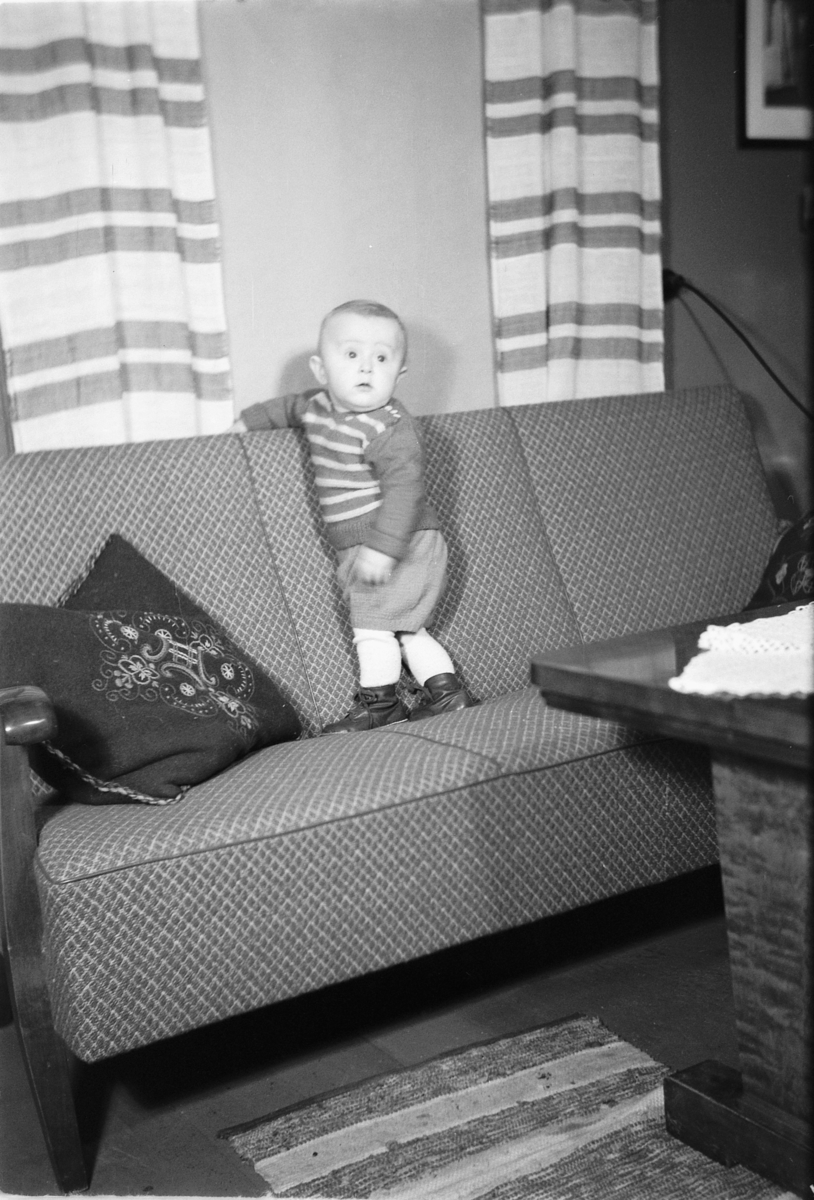 Håkon Prestkværn, Interiør, stue. Baby i en sofa.